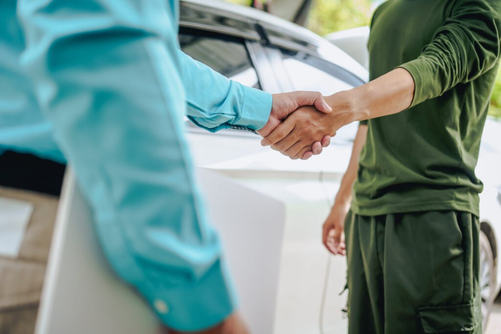 Deux personnes se serrent la main devant une voiture, symbolisant un accord ou la résolution d’un litige automobile.