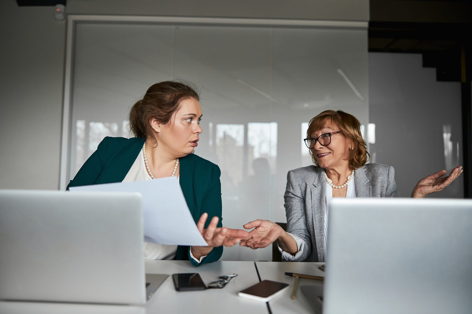 Deux femmes d’affaires discutant avec des expressions de désaccord et de surprise devant leurs ordinateurs portables.