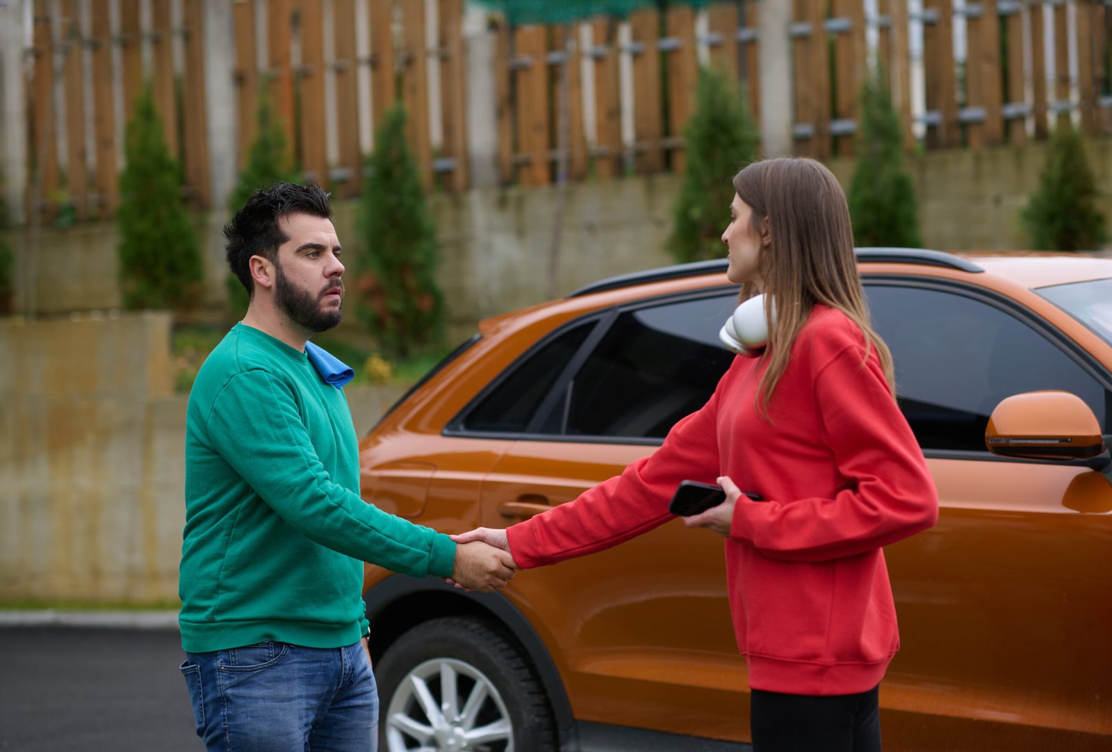 Un homme et une femme se serrent la main devant un SUV orange, symbolisant un accord automobile.