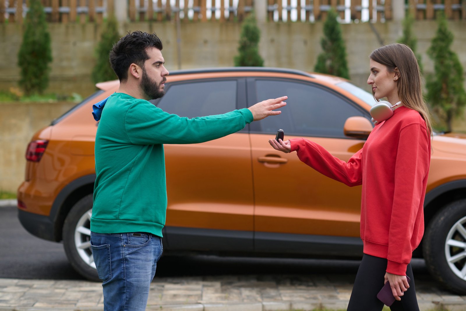 Un homme tend la main pour recevoir les clés de voiture d'une femme devant un SUV orange.