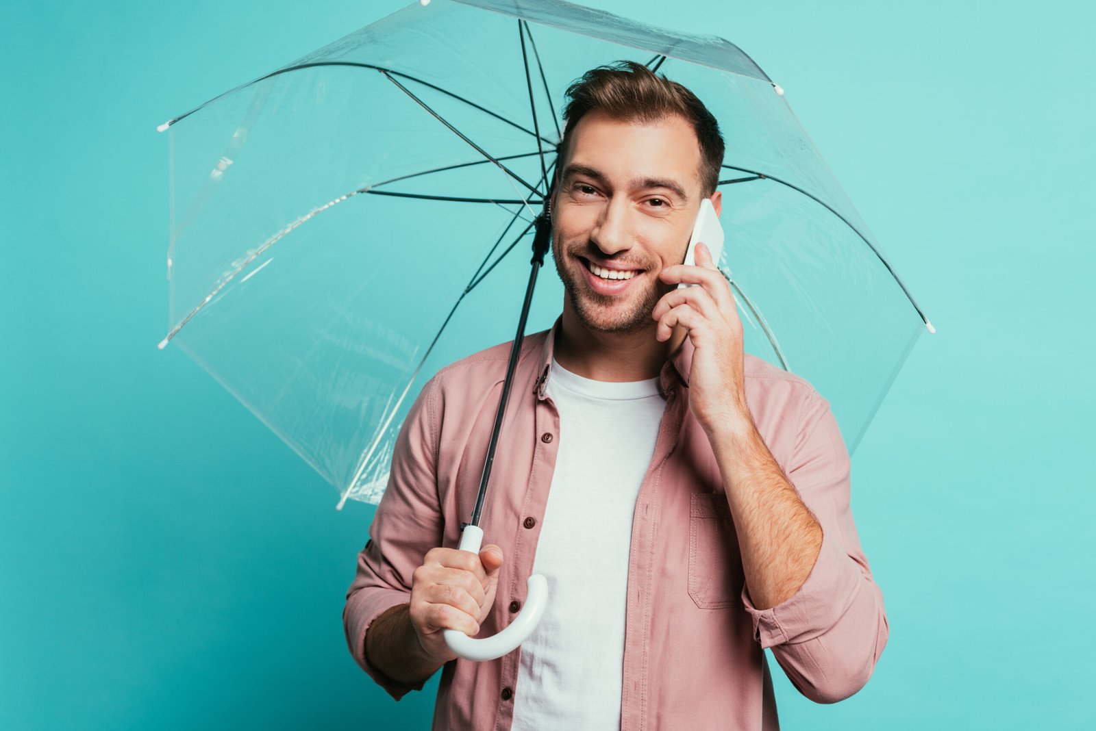 Homme souriant tenant un parapluie transparent tout en parlant au téléphone.