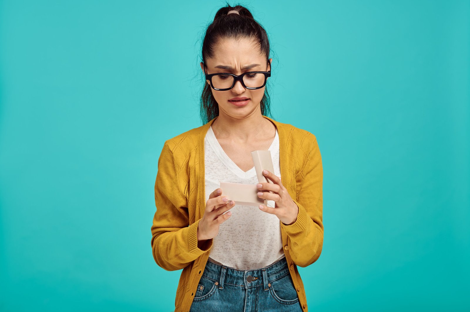 Jeune femme inquiète portant des lunettes et un gilet jaune, lisant un document avec une expression de déception.
