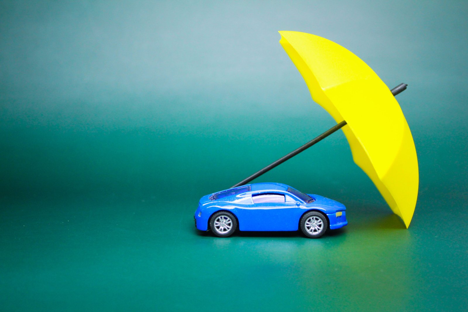 Une petite voiture bleue protégée par un parapluie jaune symbolisant l'assurance automobile.