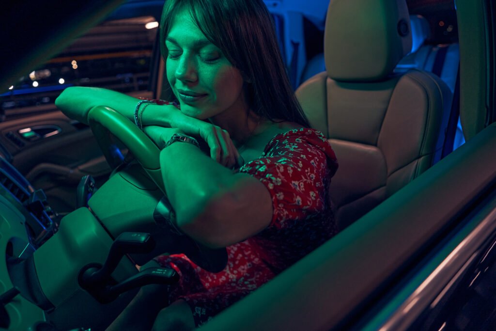 Femme assise au volant d’une voiture, les yeux fermés et la tête reposée sur le volant.